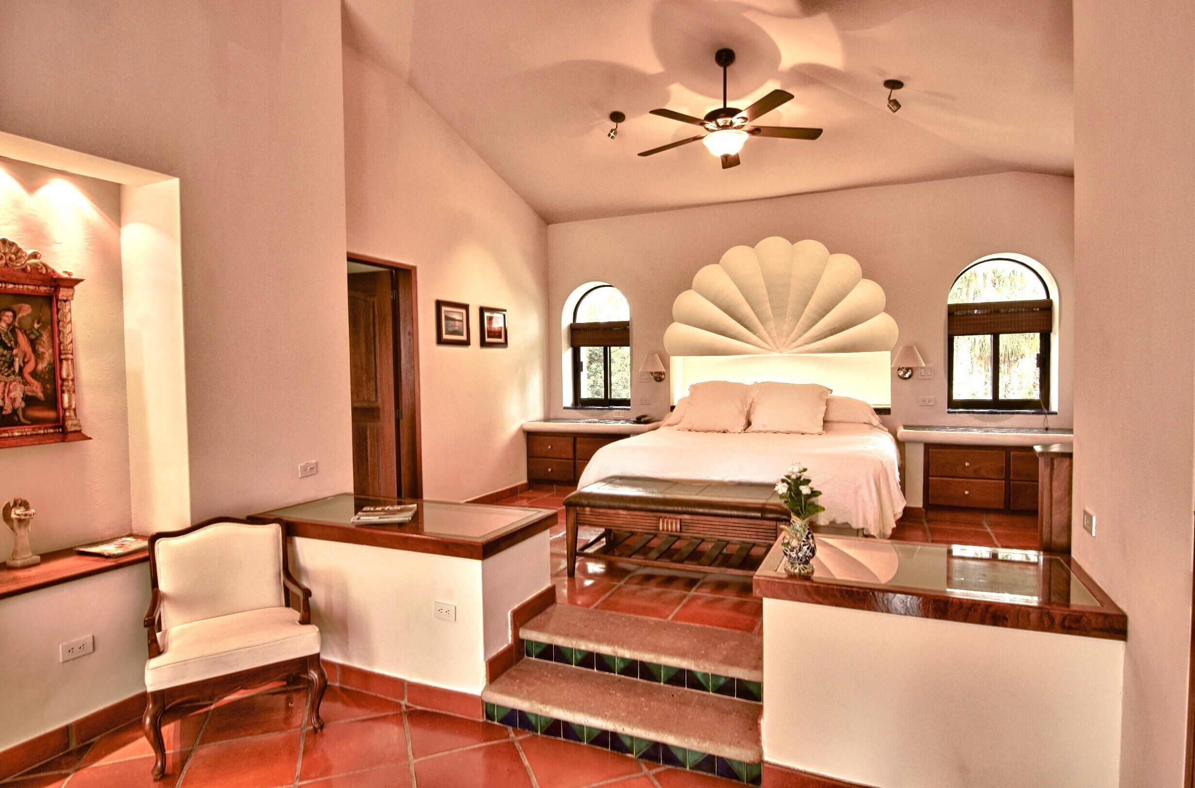 A bedroom with a large bed, a chair, a desk, and a ceiling fan.