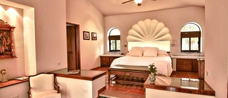 A bedroom with a large bed, a chair, a desk, and a ceiling fan.
