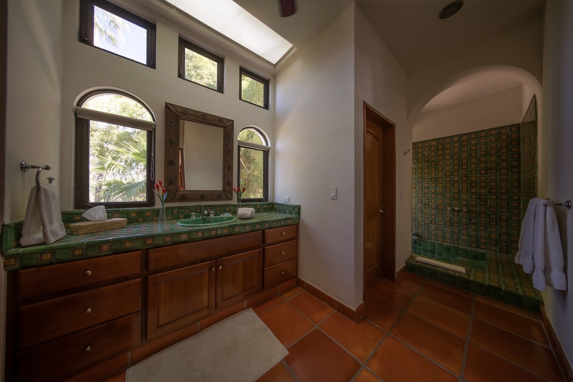 Une salle de bain avec un lavabo recouvert de carreaux verts, des meubles en bois et un grand miroir.