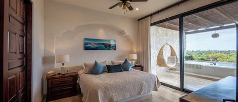 A bedroom with a bed, nightstands, a ceiling fan, a large window with a view, and a hanging chair.