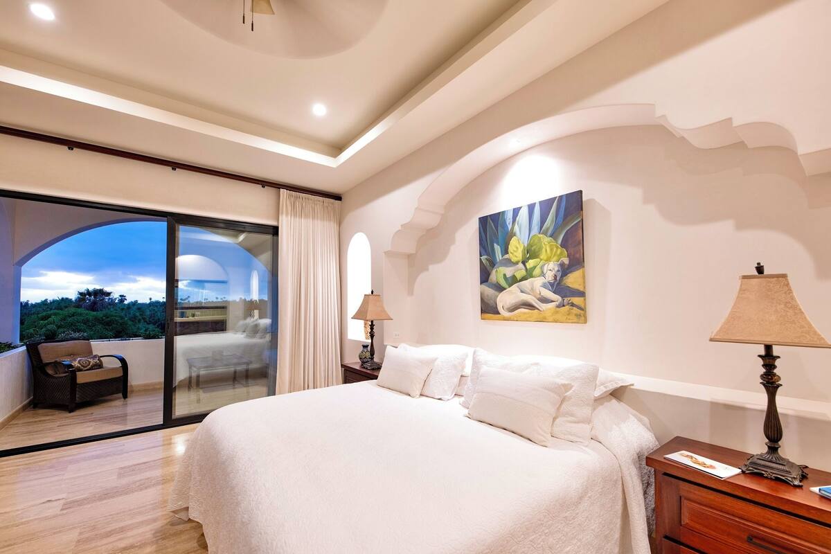 Een ruime slaapkamer met een groot bed, een glazen deur naar een balkon en een schilderij aan de wand.