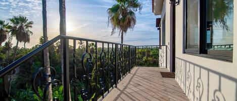 A balcony with a wrought iron railing, a view of palm trees, and a building with large windows.