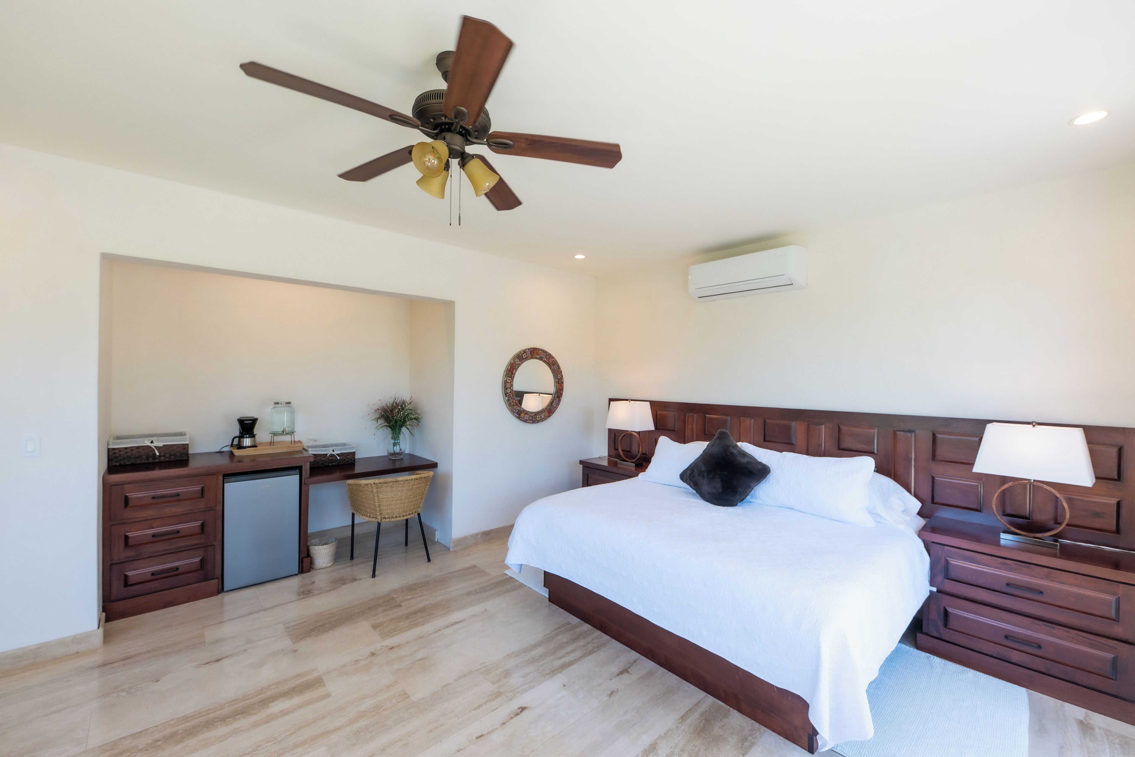 Une chambre à coucher comprenant un lit, un bureau, une chaise, un ventilateur de plafond et un climatiseur fixé au mur.