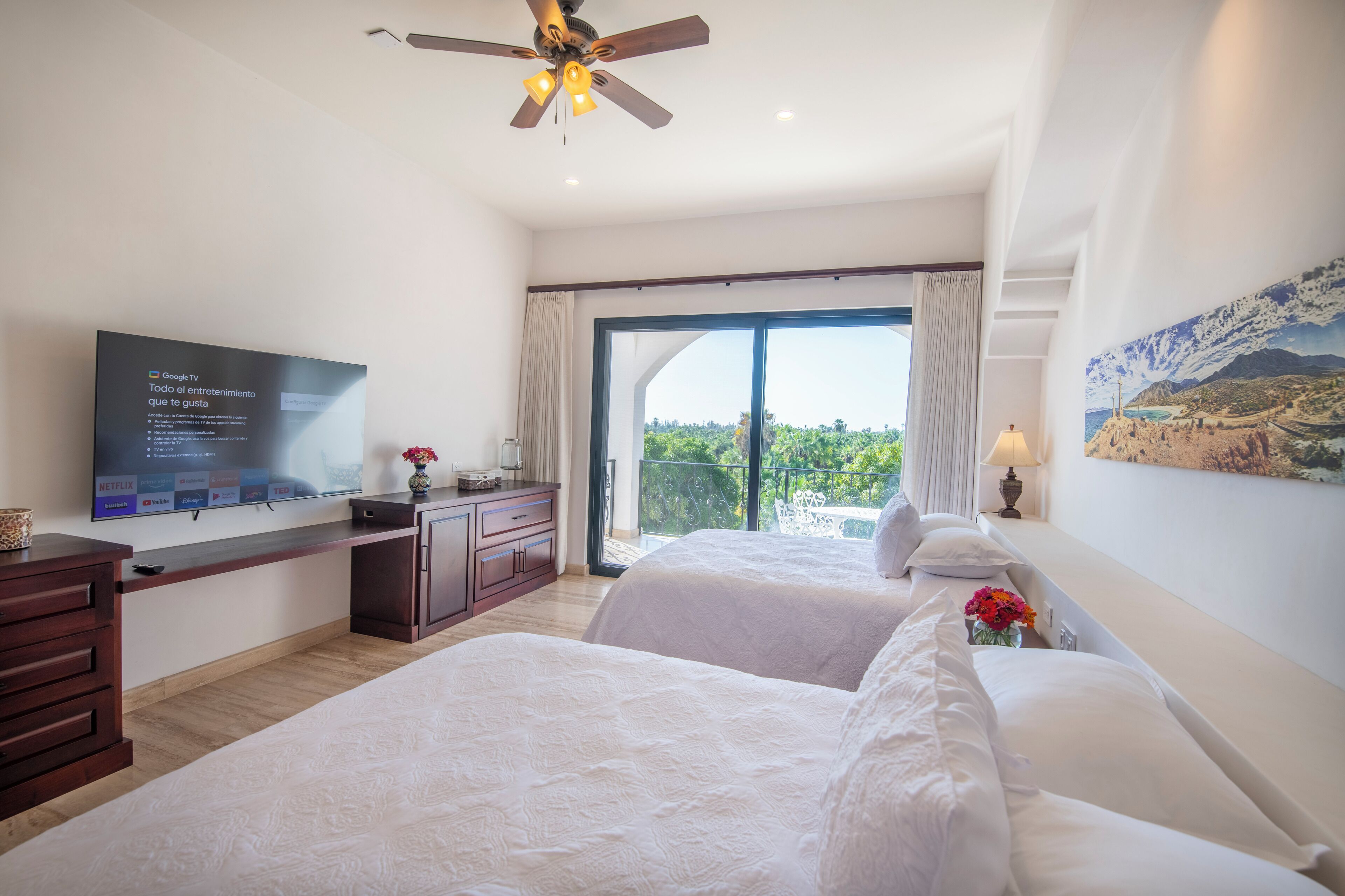 Habitación de hotel con un televisor grande, balcón con vistas y ventilador de techo.