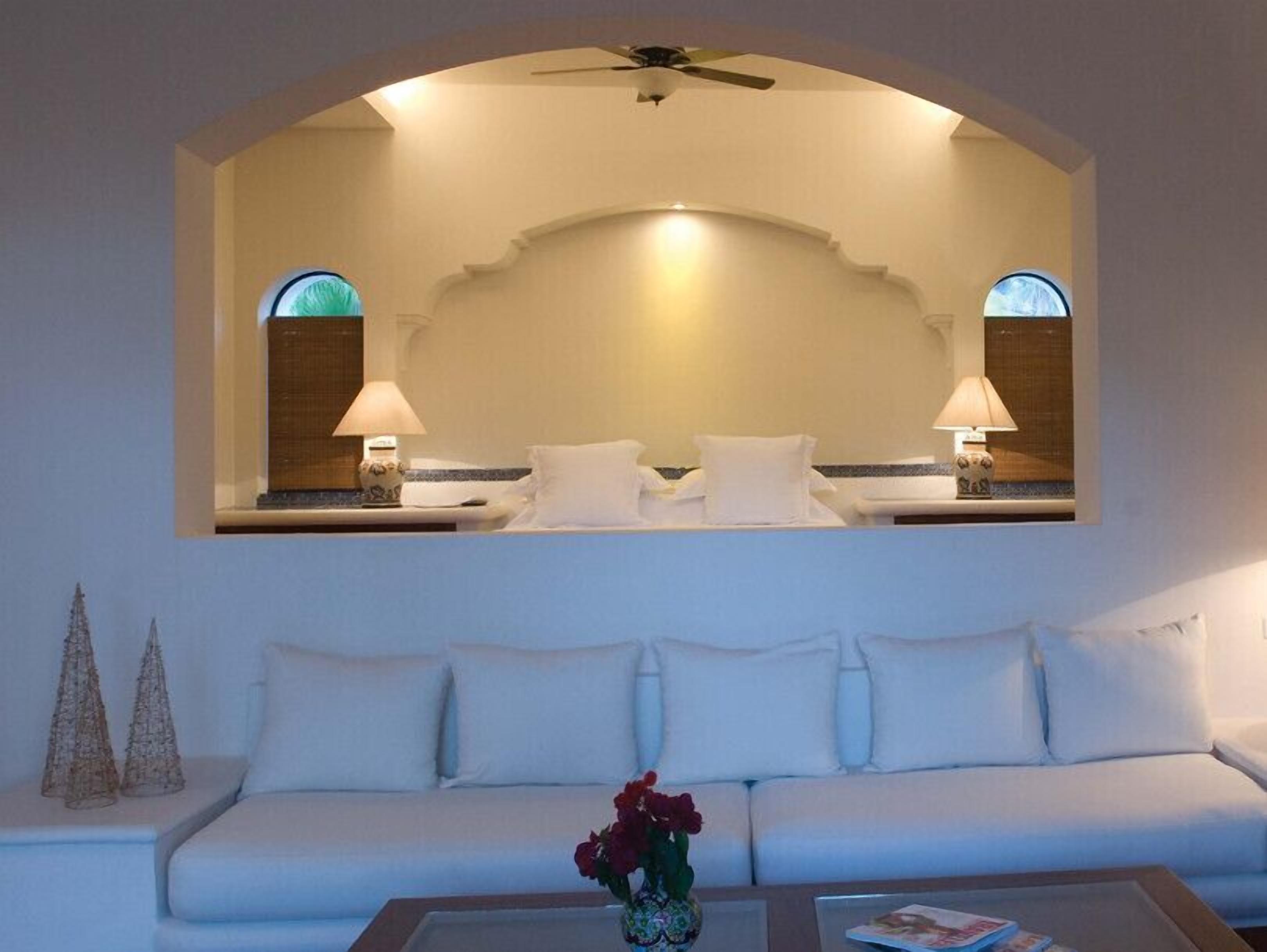 A hotel room with a white sofa, a coffee table with a vase of flowers, and a large mirror above the bed.