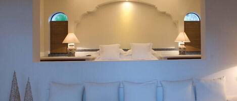 A hotel room with a white sofa, a coffee table with a vase of flowers, and a large mirror above the bed.
