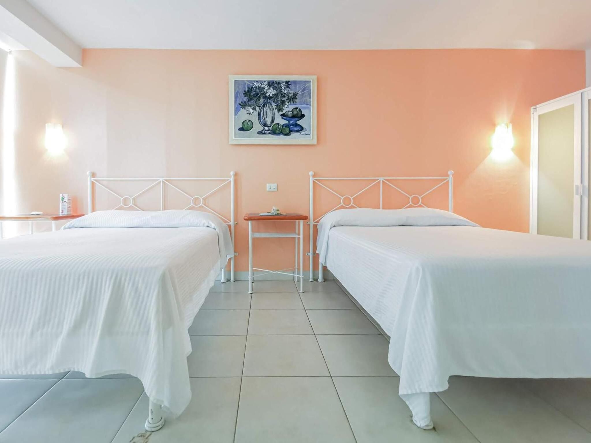 Une chambre d’hôtel avec deux lits, une petite table, un tableau au mur et une table de chevet avec une lampe.
