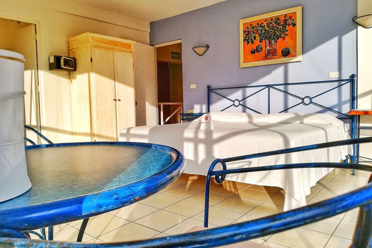 A bedroom with a bed, a table with a blue top, a wardrobe, and a painting on the wall.