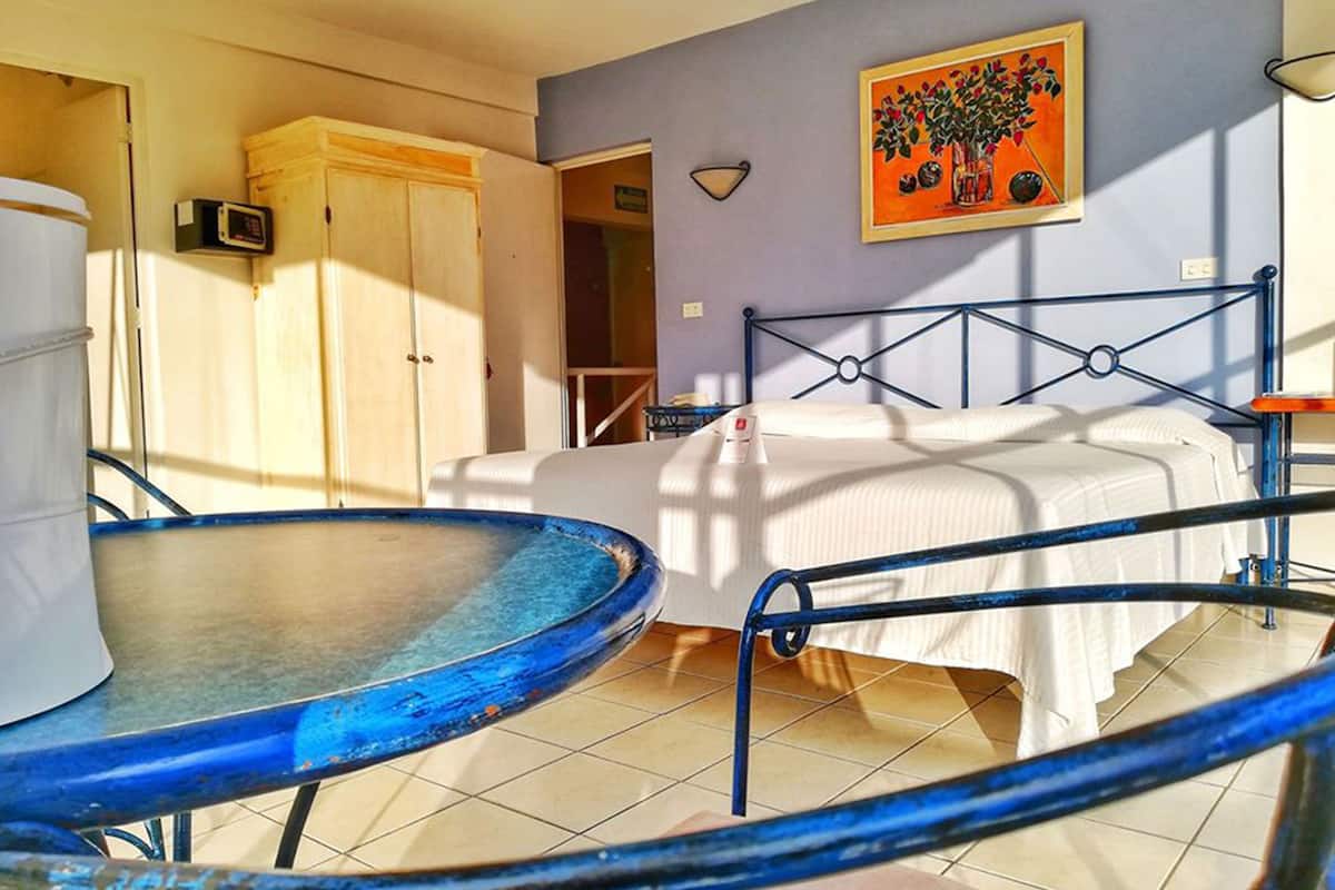 A room with a bed, a table with a blue surface, a white cabinet, and a painting on the wall.