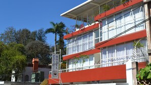 Un hotel con fachada roja, balcones con plantas y un cielo azul despejado.