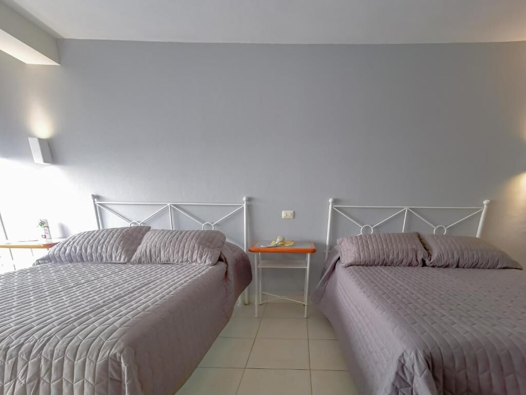 A hotel room with two beds, a small table, and a wall-mounted light fixture.