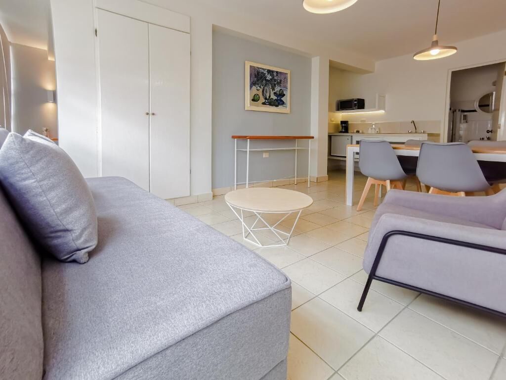 En moderne stue med en grå sofa, et rundt sofabord og et spiseområde med stole.