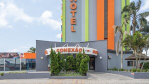 Entrada de un hotel con diseño moderno, destacándose un cartel que dice "HOTEL CONEXÃO".