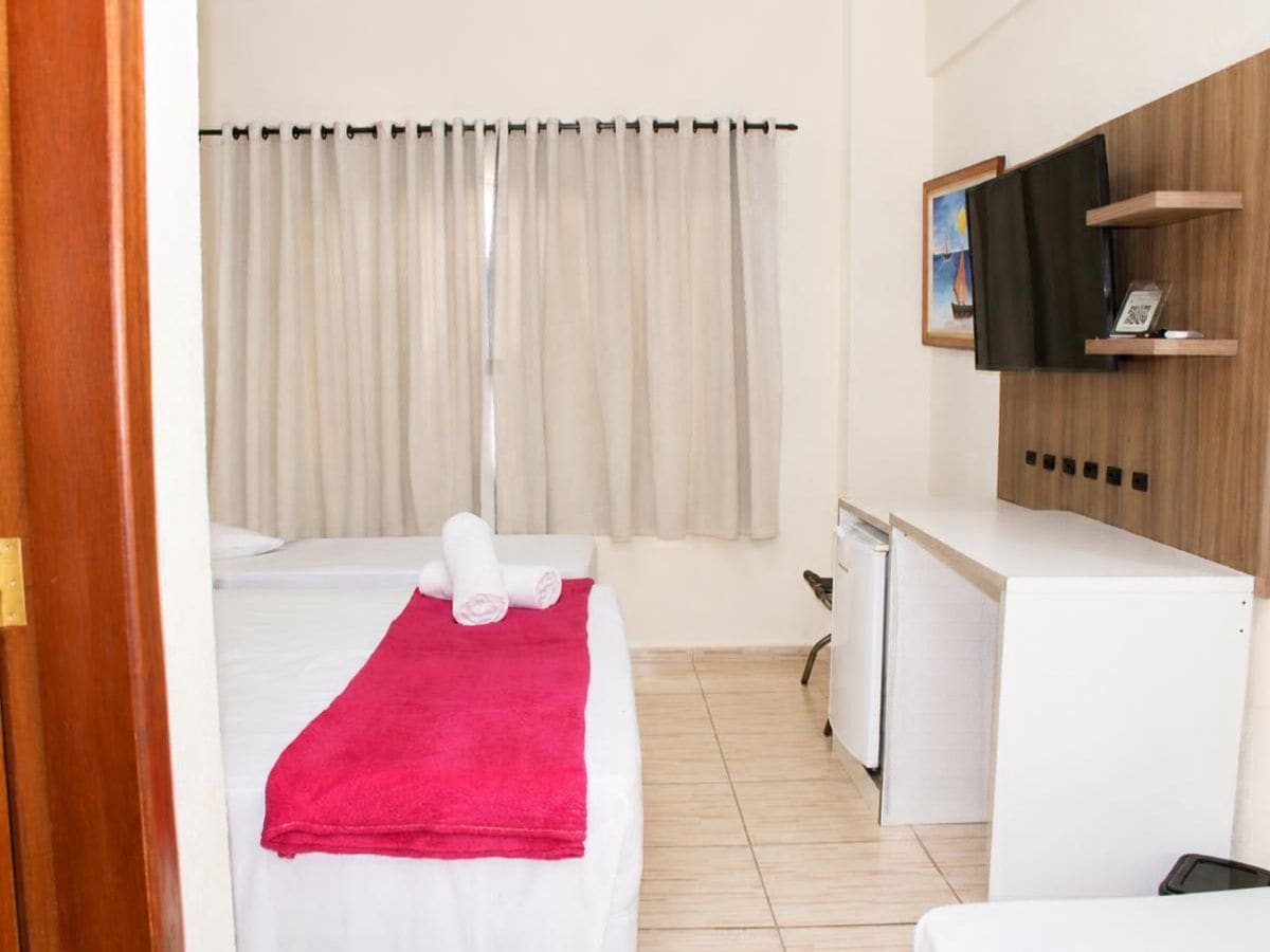 Una camera d'albergo con un letto, una scrivania, una sedia, un televisore e una finestra con tende.