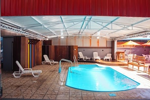 An indoor swimming pool with a tiled floor, lounge chairs, and a covered seating area. - Hotel Conexão (Penha)