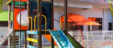 Un parque infantil con tobogán, estructuras para escalar y una zona de descanso cubierta.