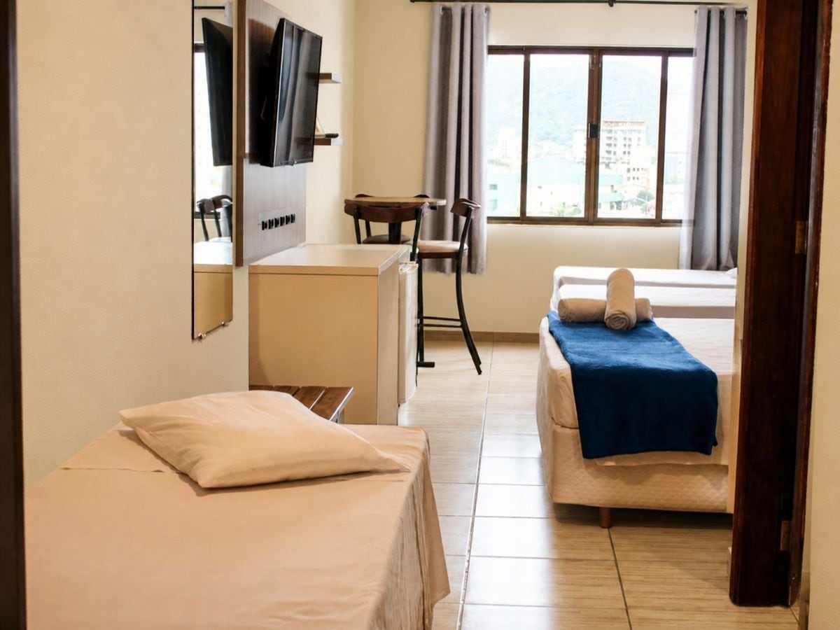 Ein Hotelzimmer mit zwei Betten, einem Schreibtisch, einem Stuhl, einem Fernseher und einem Fenster mit Vorhängen.