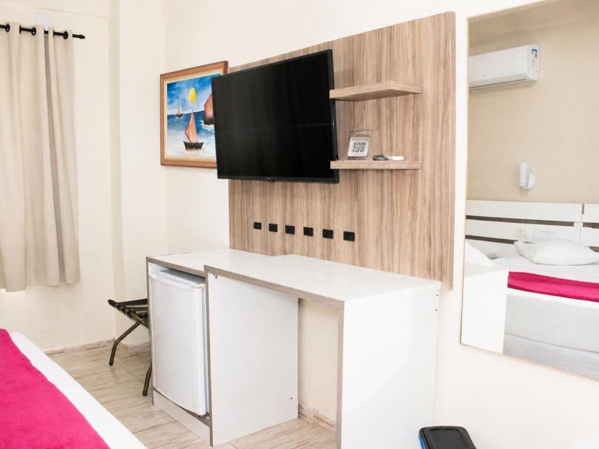 Habitación de hotel con una cama, un escritorio con televisor, un refrigerador pequeño y un cuadro en la pared.