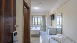 A hotel room with a bed, a desk, a TV, and a window with curtains. - Hotel Conexão (Penha)