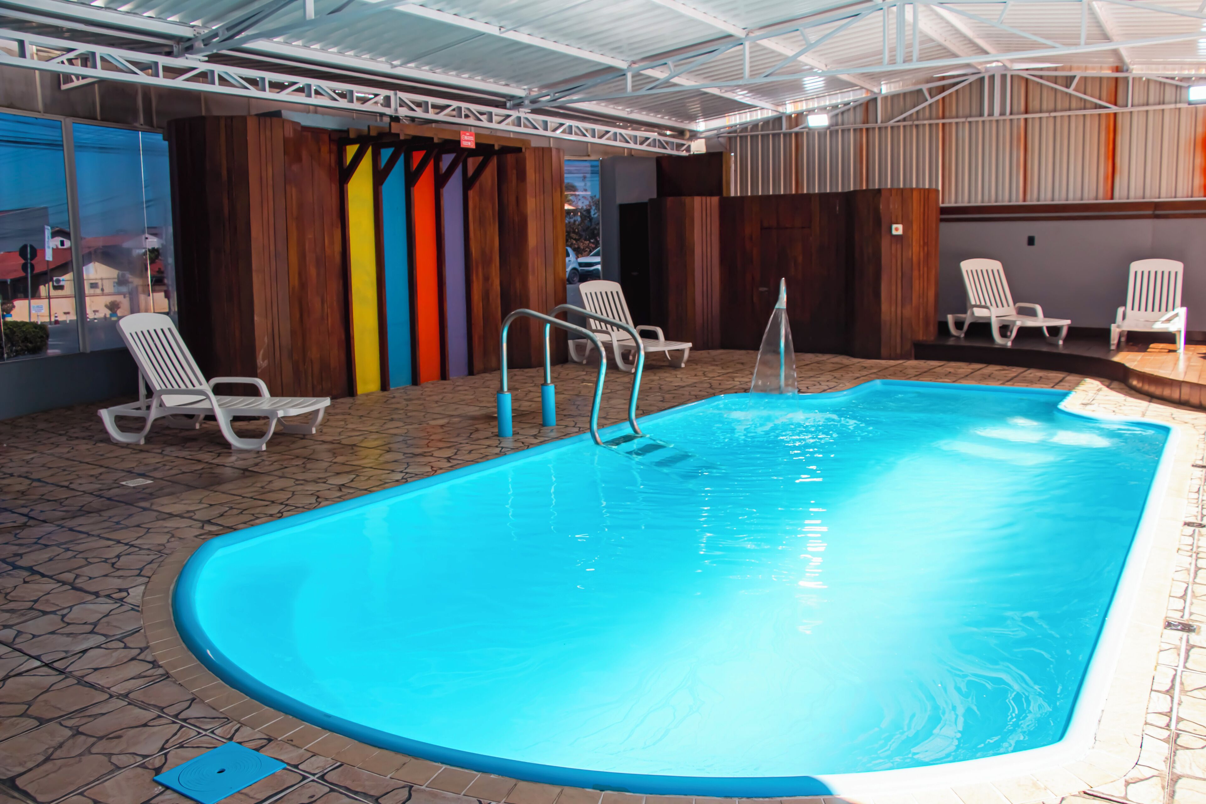 Uma piscina interior com água cristalina, rodeada por espreguiçadeiras e um chão em mosaico.