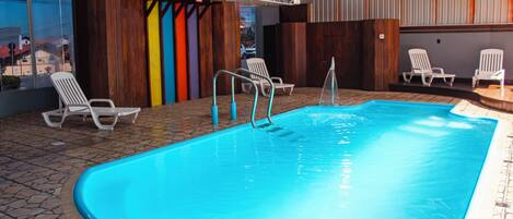 Ein Innenpool mit klarem Wasser, umgeben von Liegestühlen und einem gefliesten Boden.