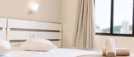 A hotel room with a bed, a window with curtains, and a wall-mounted light fixture.