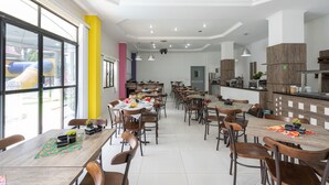 Un comedor amplio con varias mesas y sillas, ventanas grandes y una cocina al fondo.