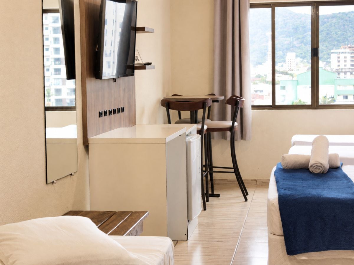 A hotel room with a bed, a desk with a chair, a television, and a window with a view of buildings.