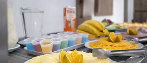 Un bufé con diversas opciones de comida, incluyendo un plato de queso en rodajas, un plátano y una bandeja de naranjas cortadas.