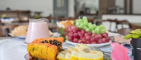 A breakfast table with a variety of fruits and a pink beverage.
