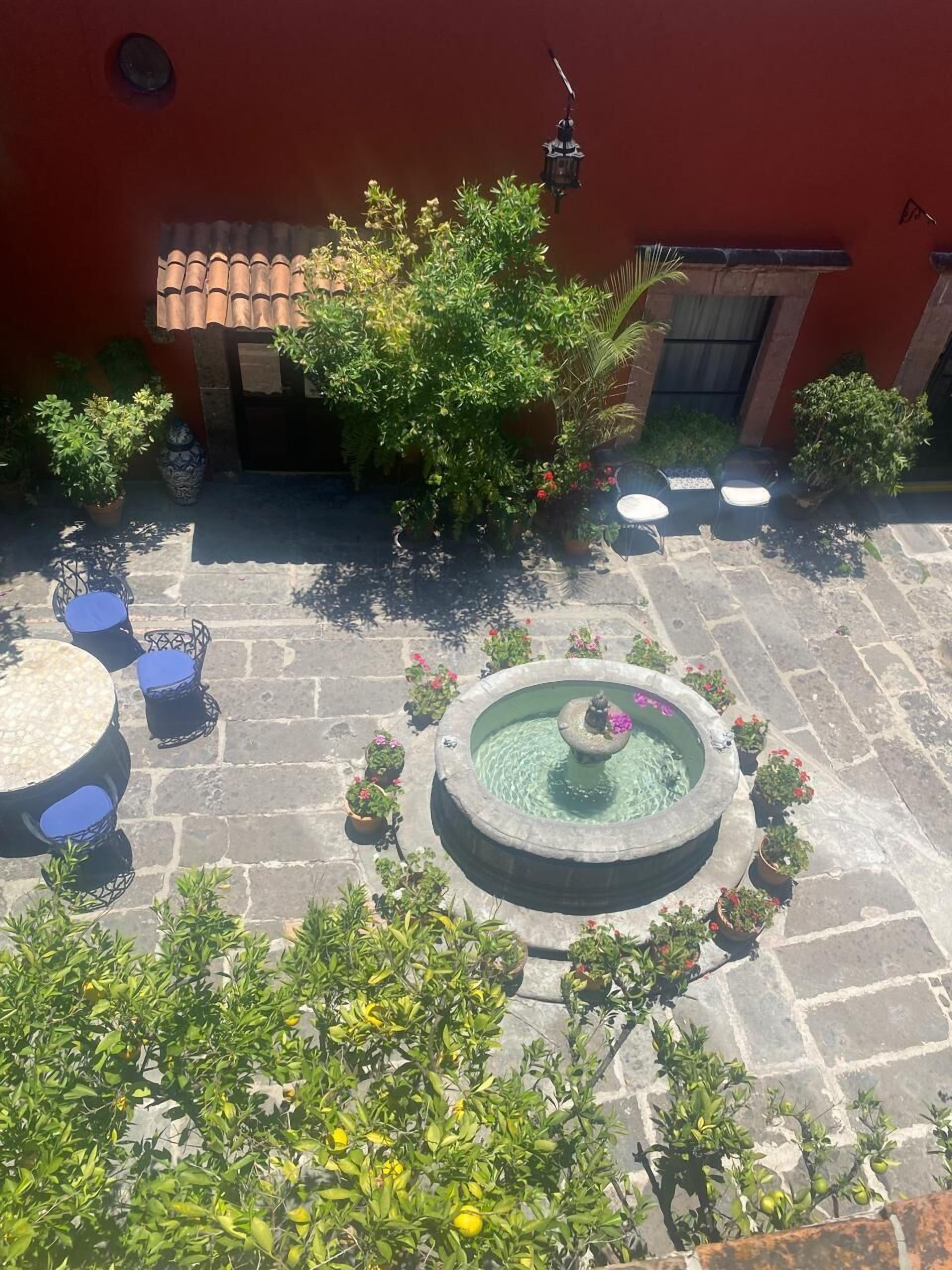 A courtyard with a fountain, potted plants, and outdoor seating.