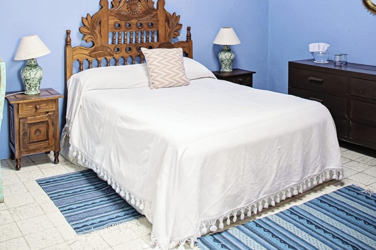 Un dormitorio con cama de madera, dos mesitas de noche, ventilador de techo y tragaluz.
