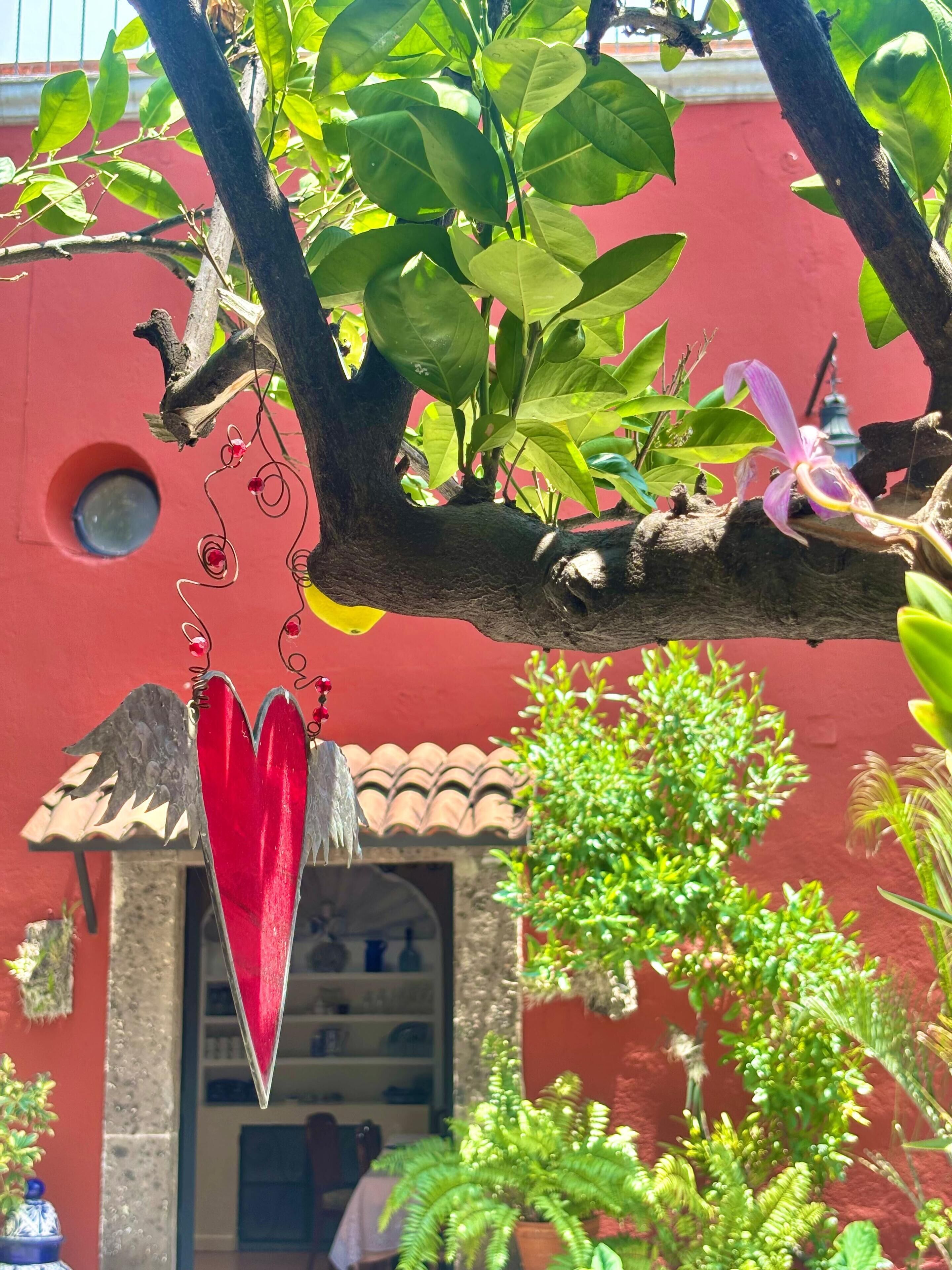 Un bâtiment rouge avec un toit recouvert de tuiles, un cœur rouge en forme d’ornement suspendu et un feuillage vert.