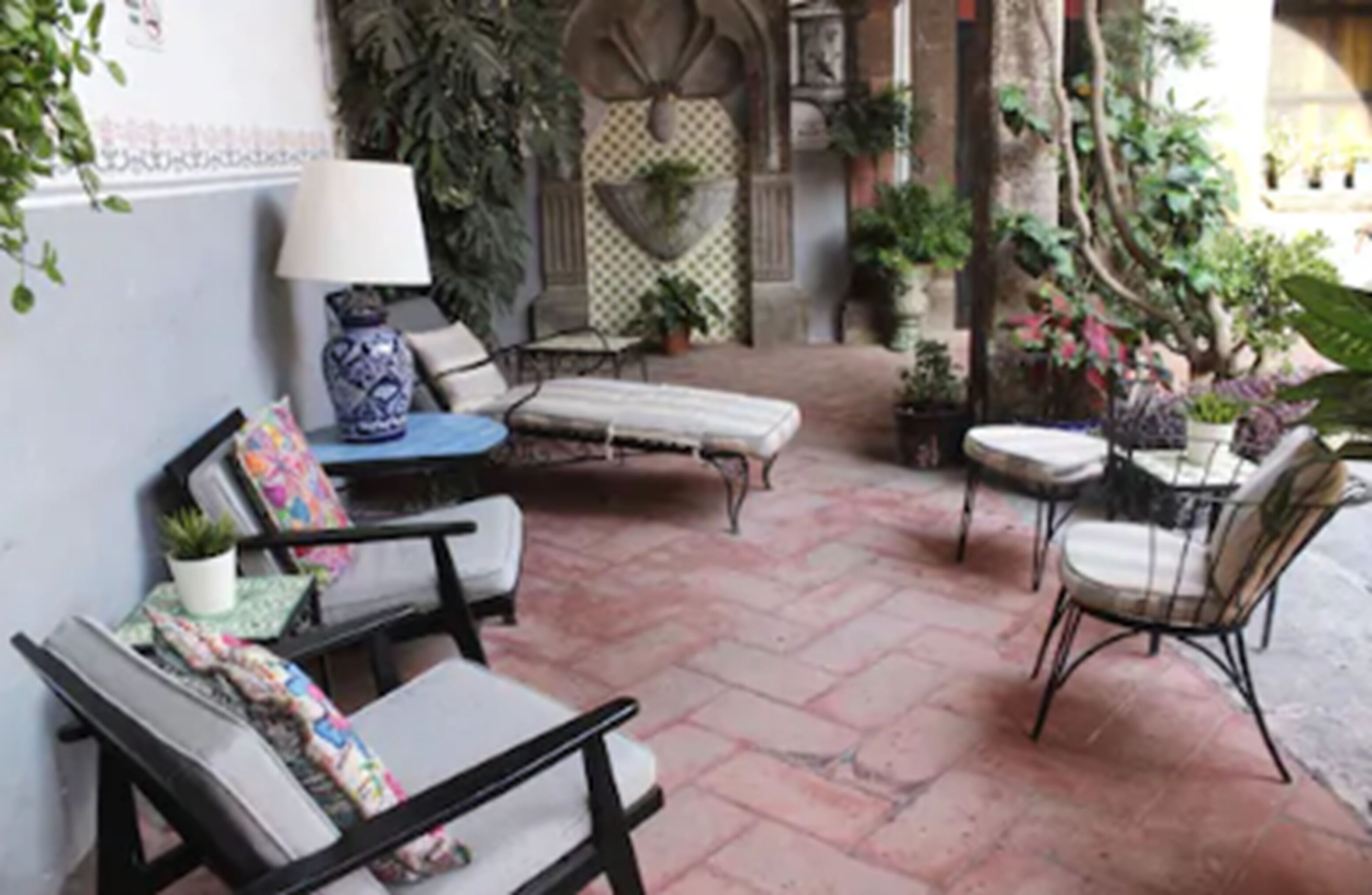 A patio area with outdoor seating, including a sofa and chairs, surrounded by potted plants and a decorative wall.
