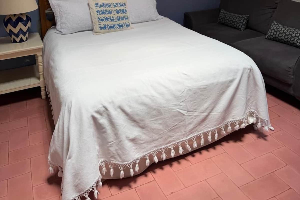 A bedroom with a bed, a nightstand, a dresser, a chandelier, and a sofa.