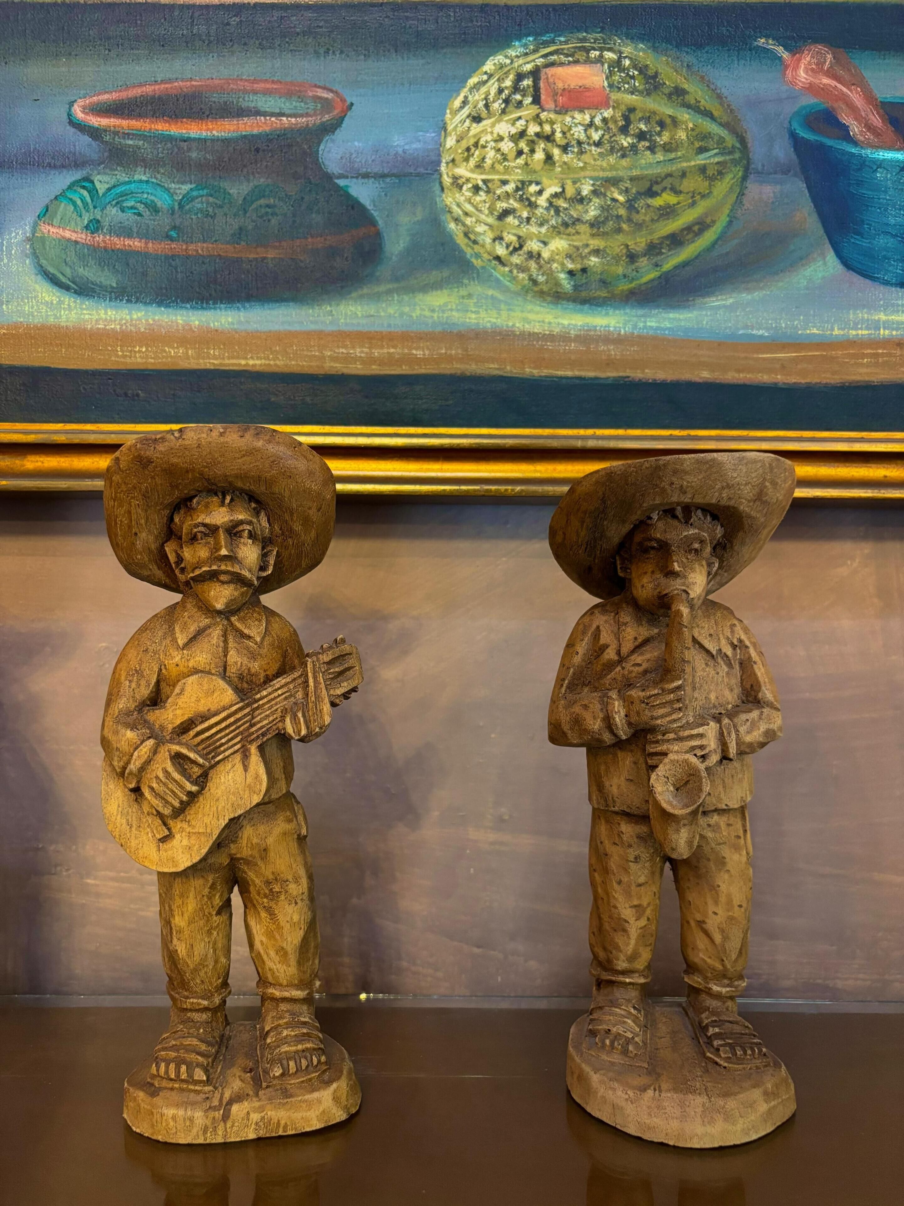 Two wooden sculptures of musicians, one playing a guitar and the other a trumpet, placed on a reflective surface.