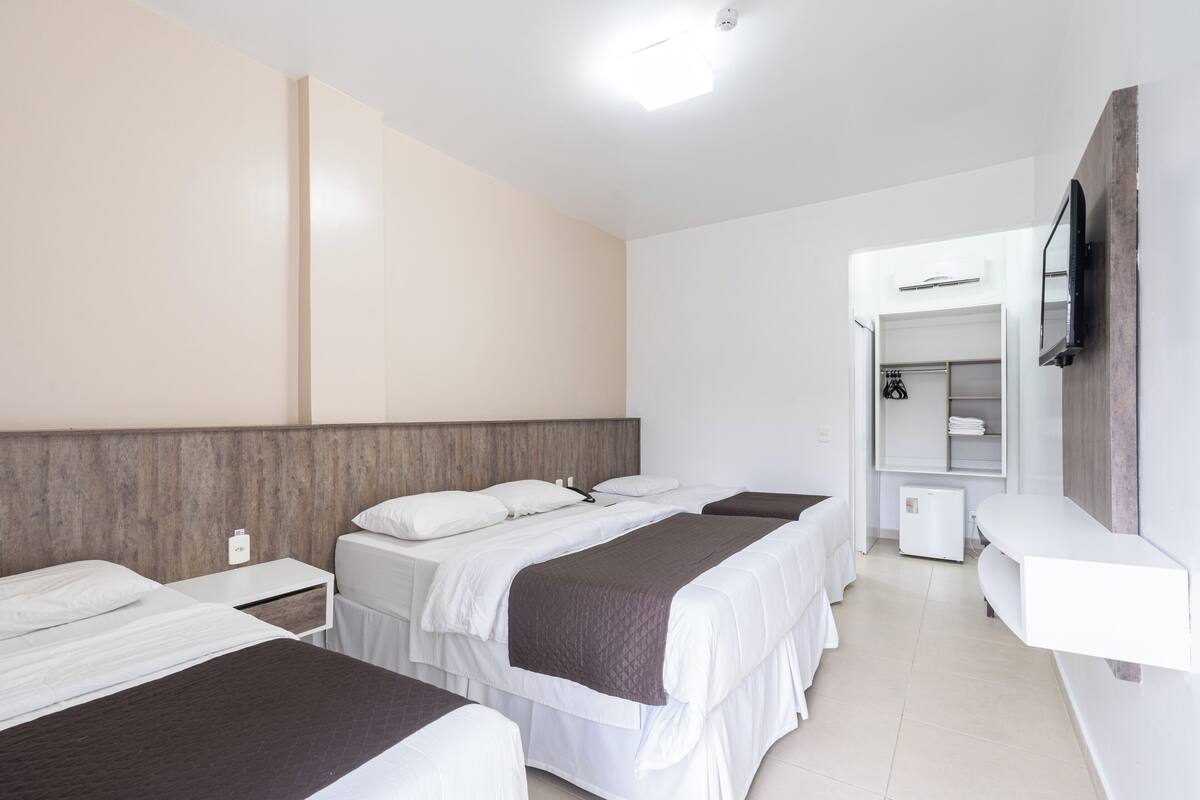 A hotel room with three beds, a wardrobe, a mirror, and a television.