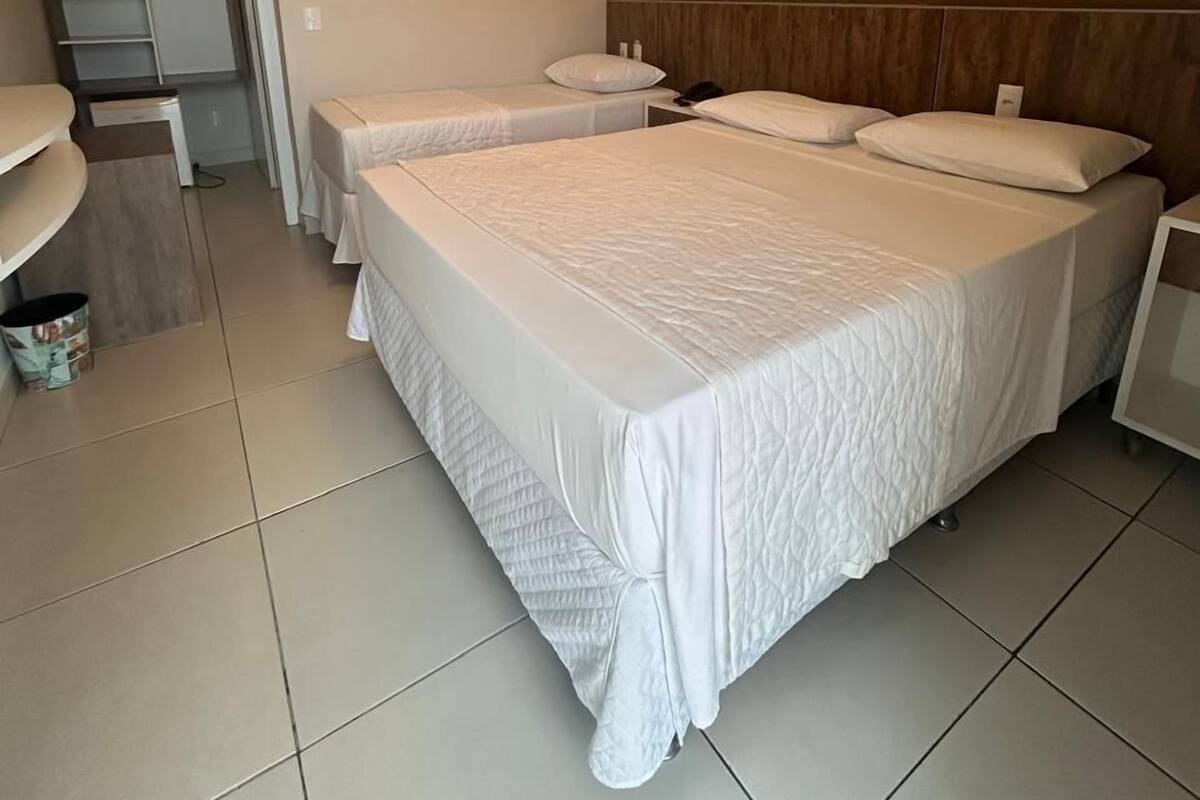 A hotel room with two beds, a small desk, and a closet with shelves.
