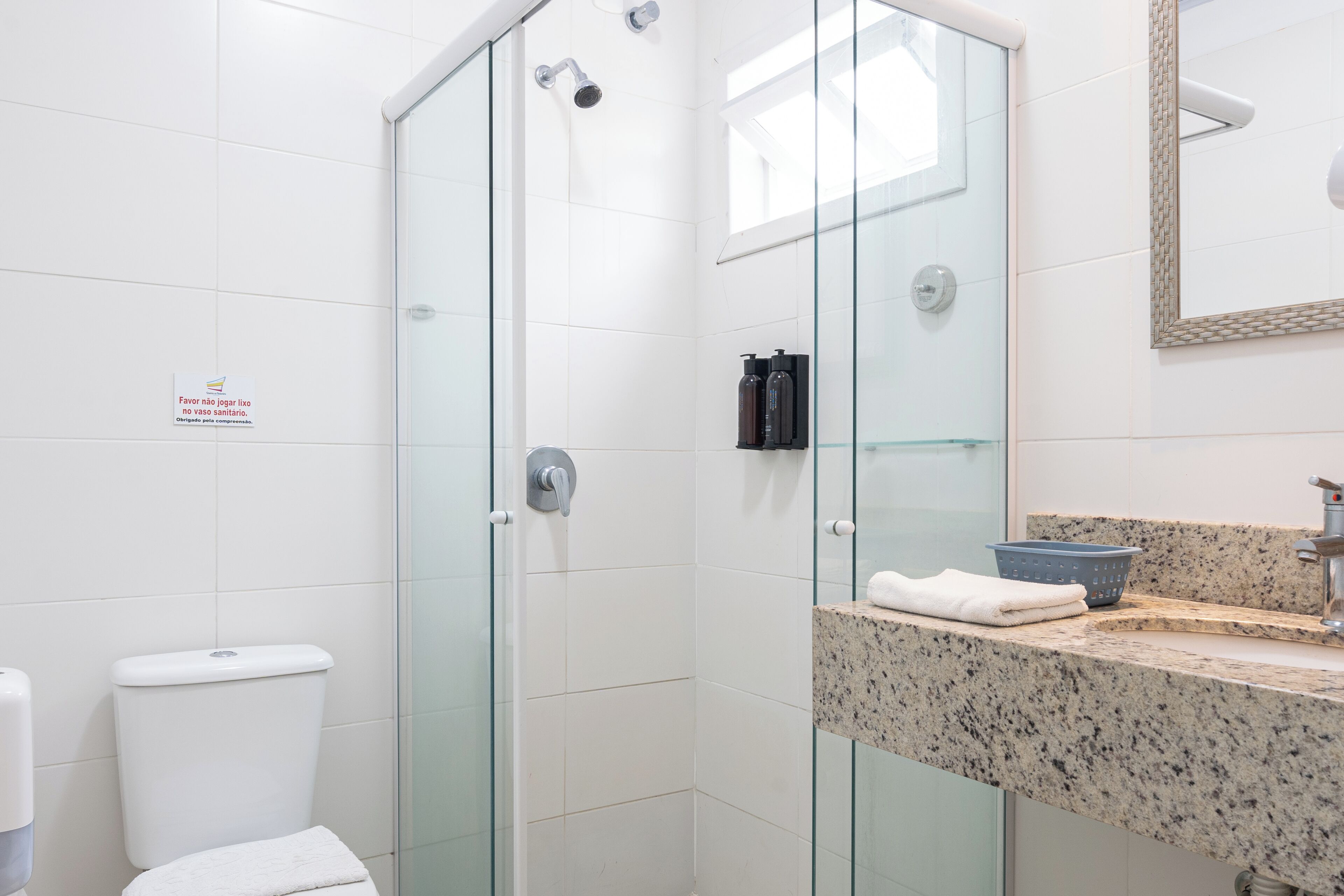 Un baño moderno con cabina de ducha de vidrio, inodoro blanco y encimera de granito con lavabo y toalla.
