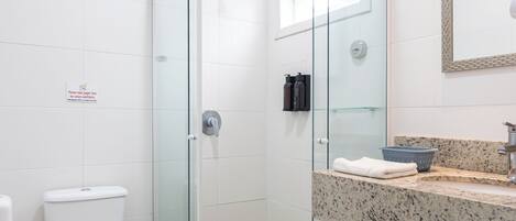 Un baño moderno con cabina de ducha de vidrio, inodoro blanco y encimera de granito con lavabo y toalla.