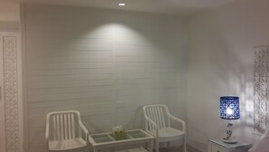 A room with white paneled walls, two white plastic chairs, a small table, and a decorative blue lamp. - P.P. Blue Sky Resort (Ko Phi Phi)