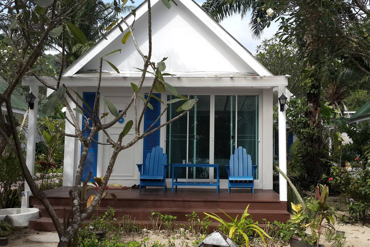 A white building with a porch, blue shutters, and a small table and bench.