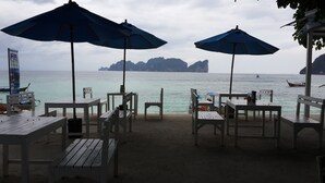 A beachside seating area with tables and chairs, umbrellas, and a view of the sea and distant islands. - P.P. Blue Sky Resort (Ko Phi Phi)