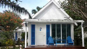 Un edificio blanco con contraventanas azules, un porche cubierto con sillas azules y una puerta con un letrero azul.