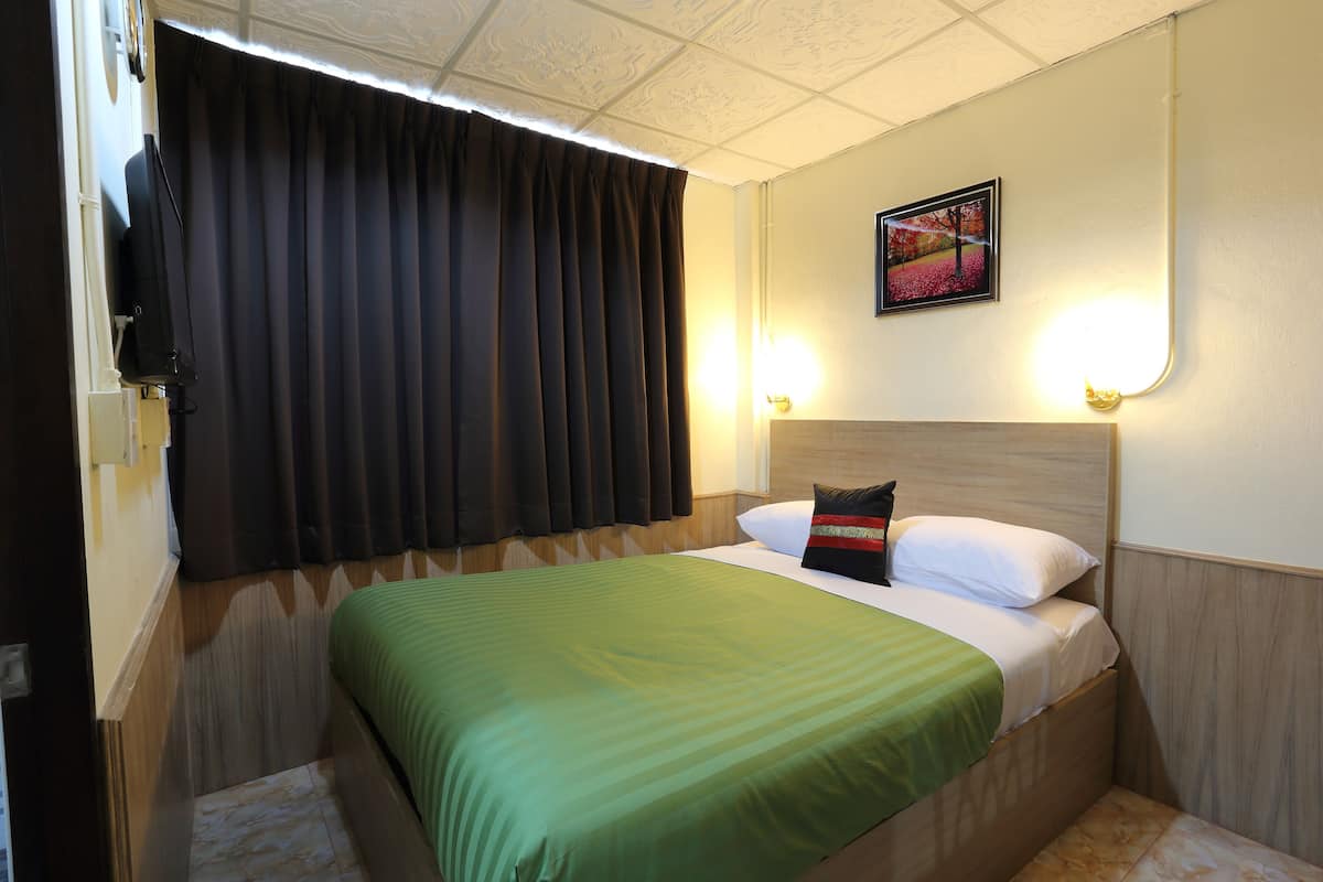 Una habitación de hotel con cama, televisor, un cuadro en la pared y ventana con cortinas.