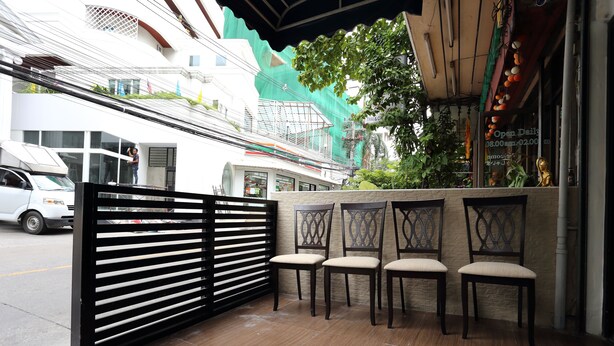 A covered outdoor seating area with four wooden chairs and a black slatted partition.