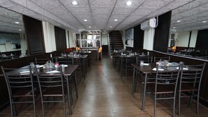 A restaurant with long tables and chairs, a staircase, and a kitchen area in the background.