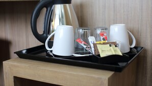 A tray with a coffee maker, two white mugs, two glasses, and some coffee packets on a wooden table.
