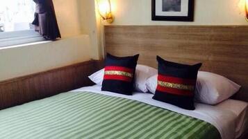 A hotel room with a bed, two pillows with red and gold stripes, a green striped bedspread, and a window with curtains.