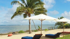 A beachside lounge area with two wooden lounge chairs and white umbrellas, overlooking the ocean. - Coral Lagoon Fiji Resort (Korolevu)